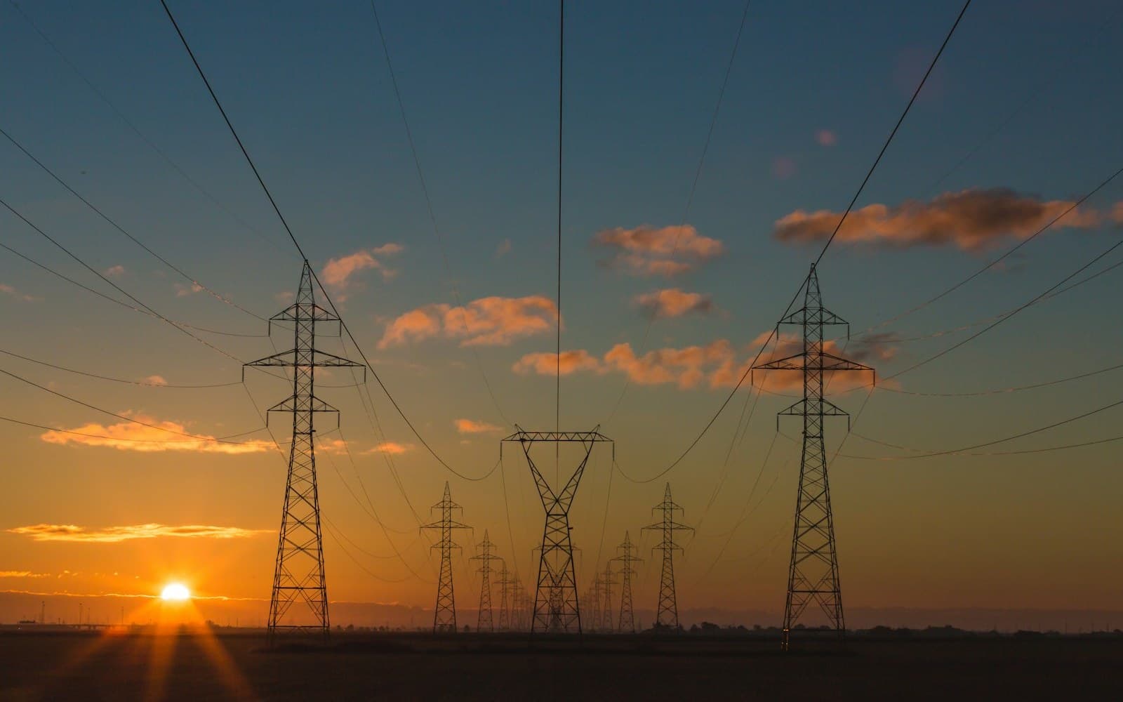 High-voltage transmission towers and power lines silhouetted at sunset